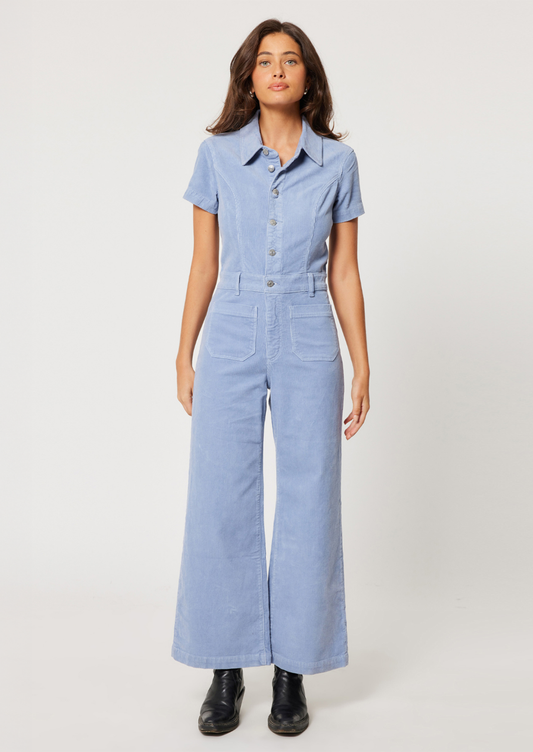 A woman wearing a corduroy one piece jumpsuit with short sleeves in periwinkle color.