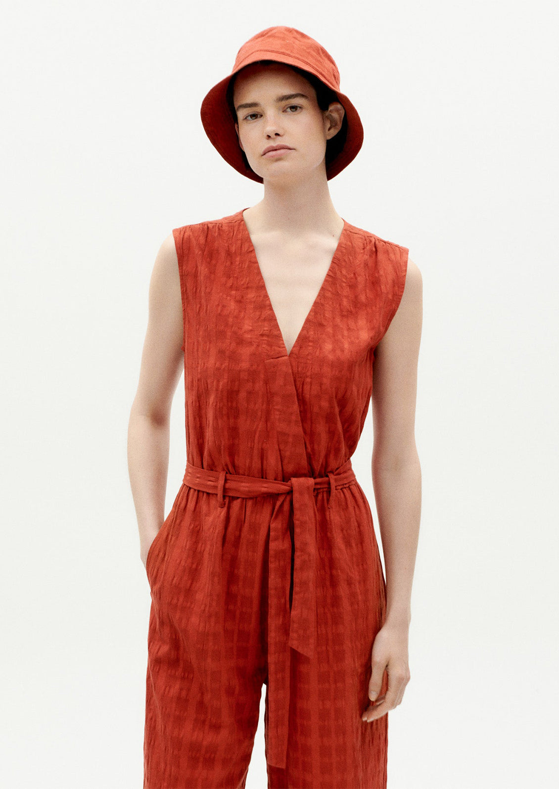 A woman wearing a rust colored jumpsuit with tie waist and tonal grid texture.