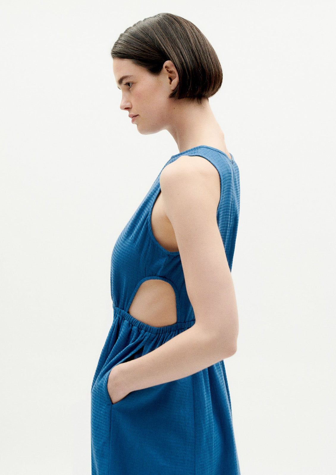A woman wearing a blue sleeveless dress with cutouts at side waist.