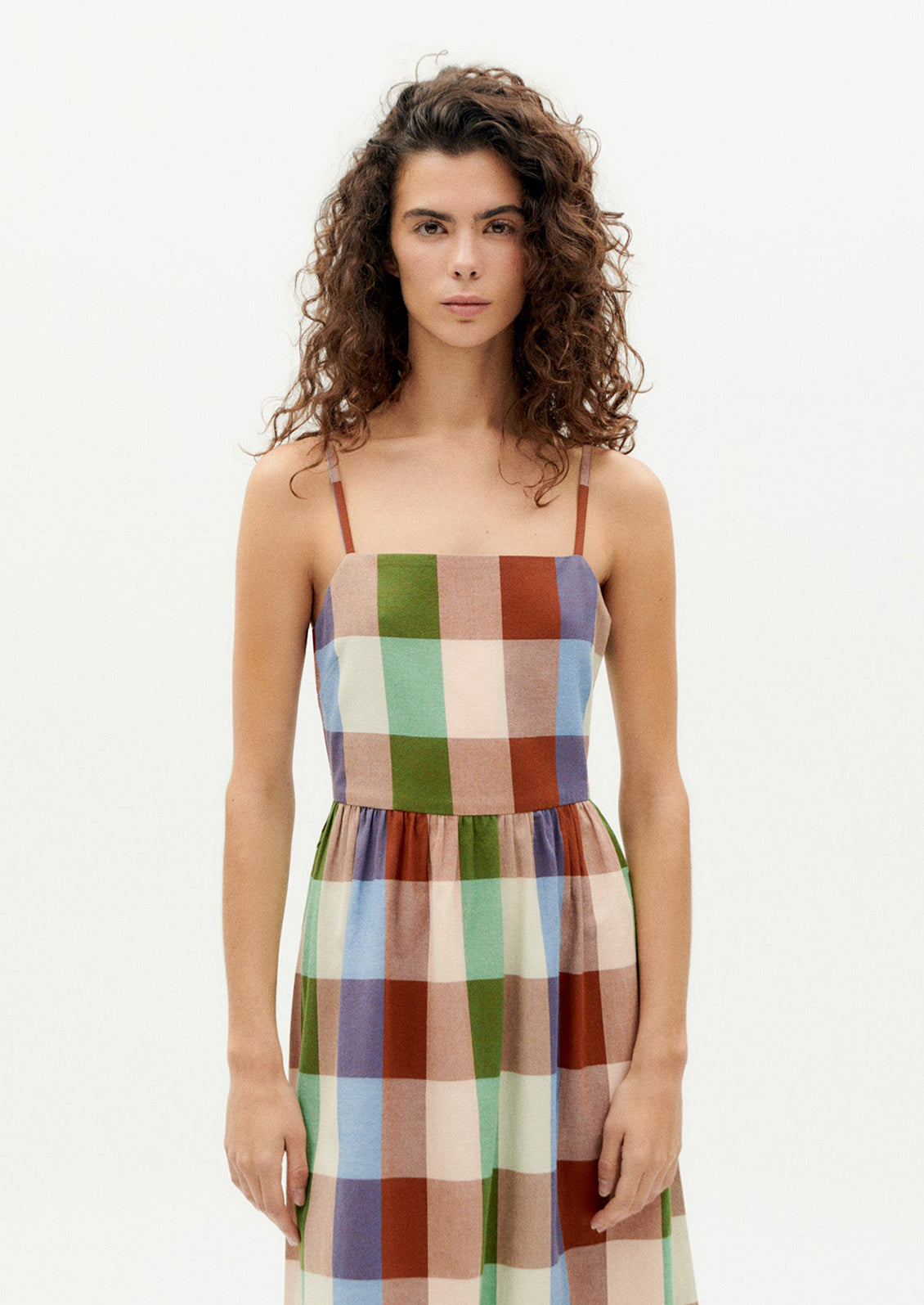 A woman wearing a thin strap dress with straight neckline, in colorful madras cotton.
