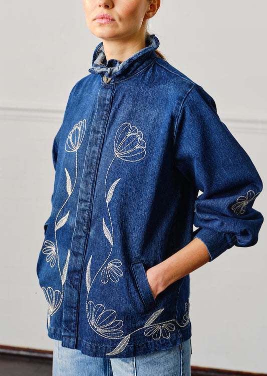 A woman wearing a blue denim jacket with white floral embroidery.