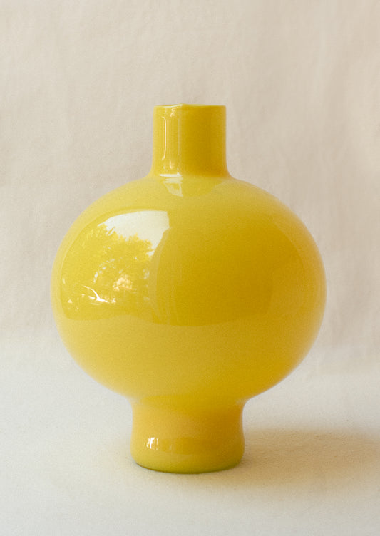 A glass vase with round, bulbous shape in opaque bright yellow hue.