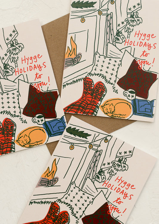 A set of cards with illustration of person sitting next to fireplace, text reads "Hygge Holidays To You!".