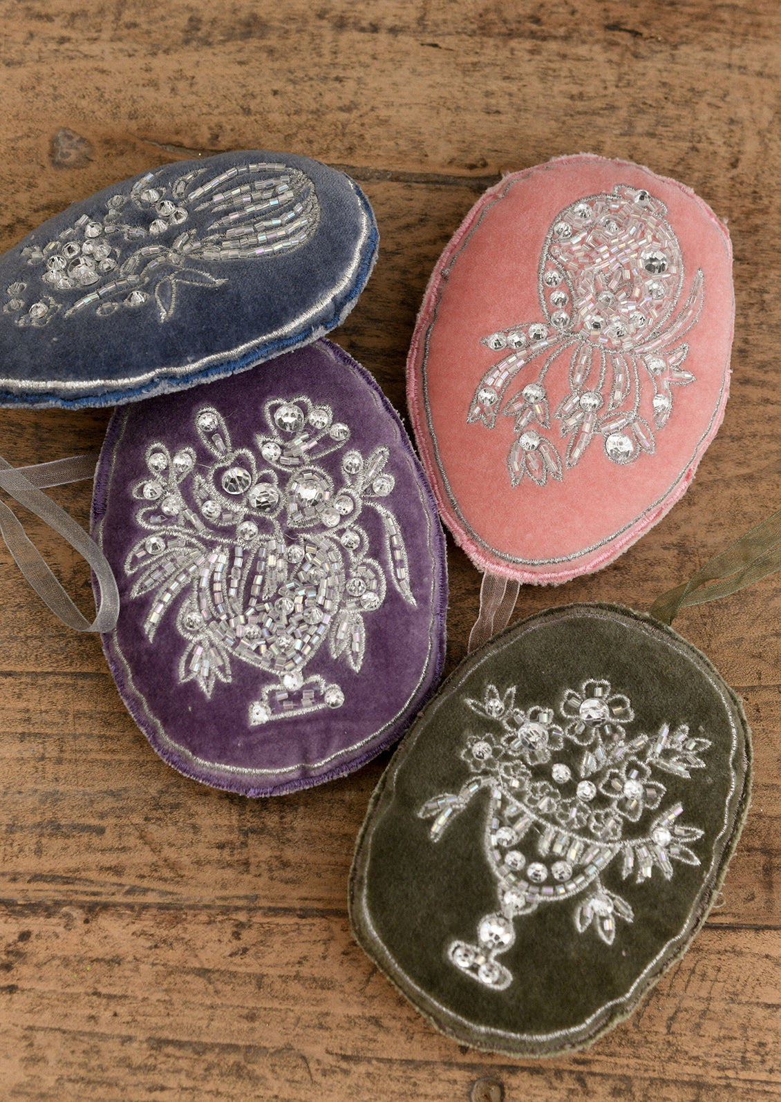 Oval shaped velvet ornaments in assorted colors with silver floral embroidery.