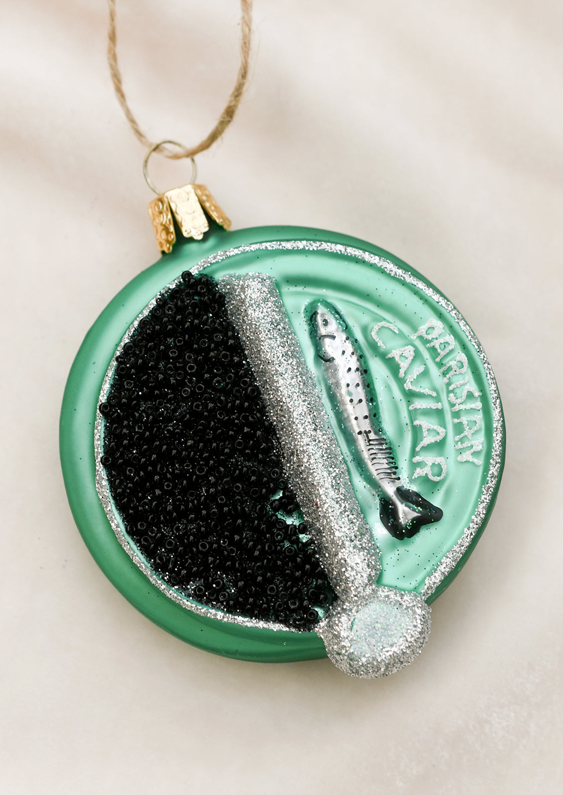 A glass ornament in the shape of round green Parisian caviar tin.