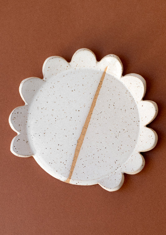 A ceramic spoon rest in speckled white with scalloped edge.