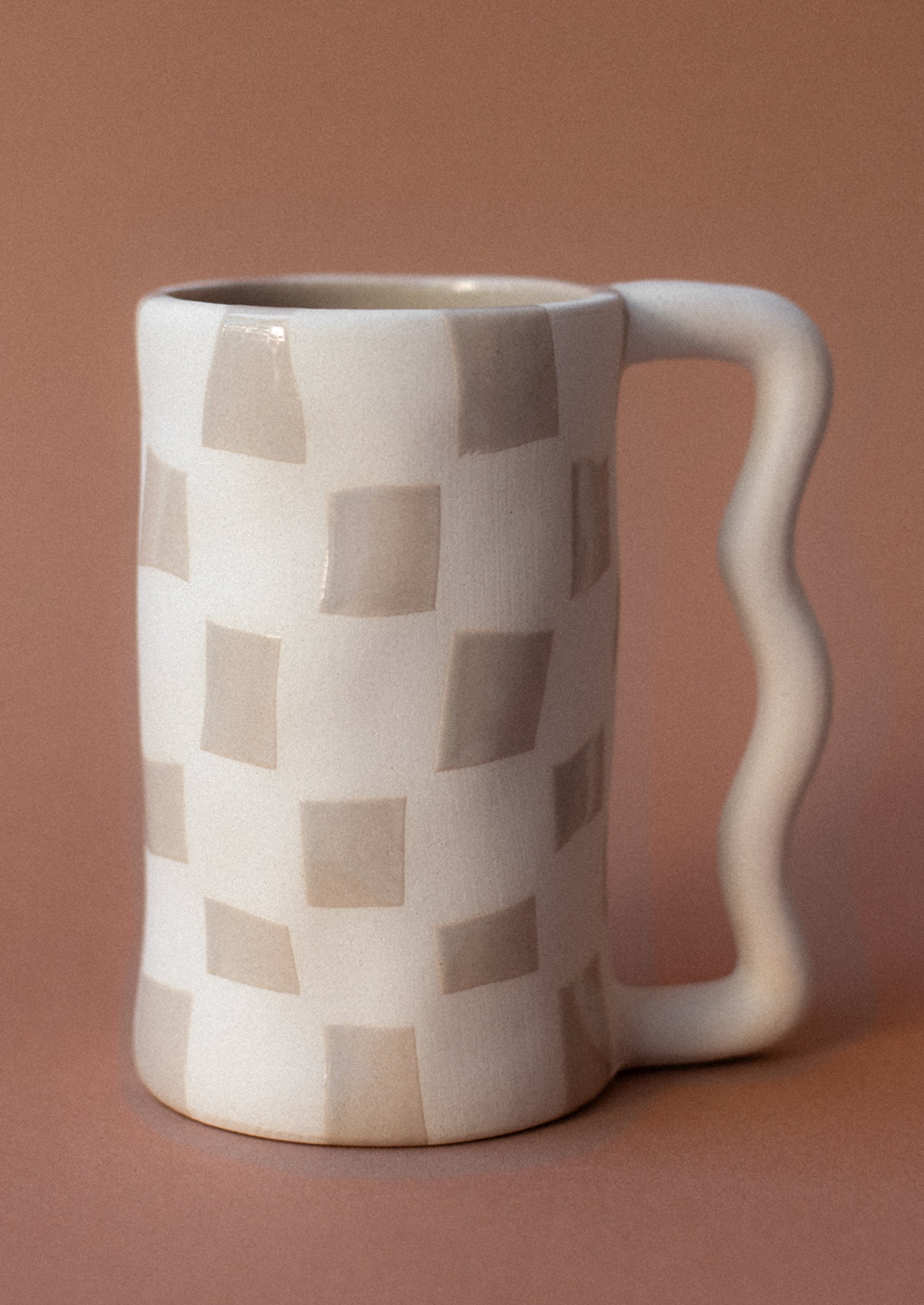 A tall white mug with taupe checker pattern and wavy handle.