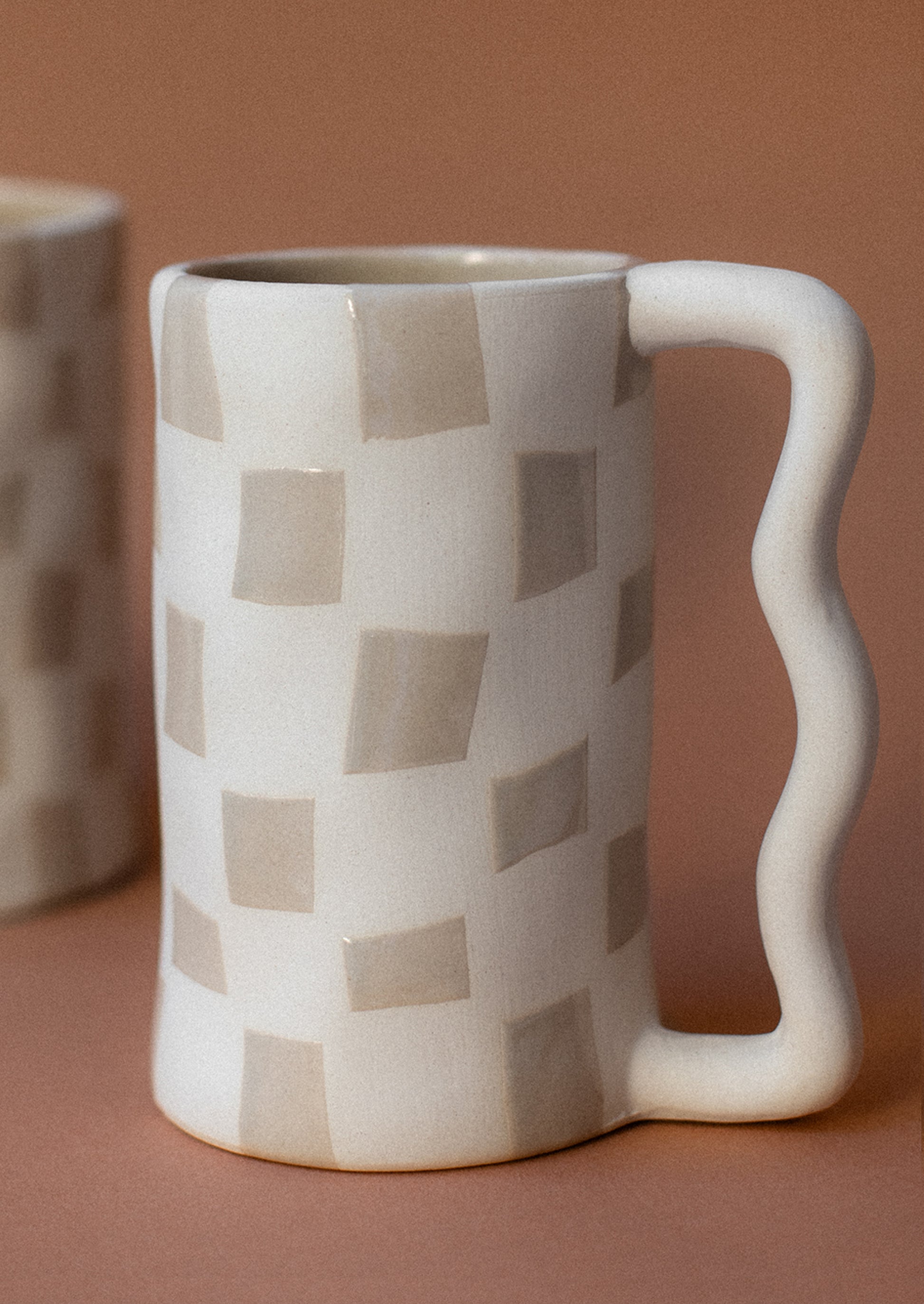 A tall white mug with taupe checker pattern and wavy handle.