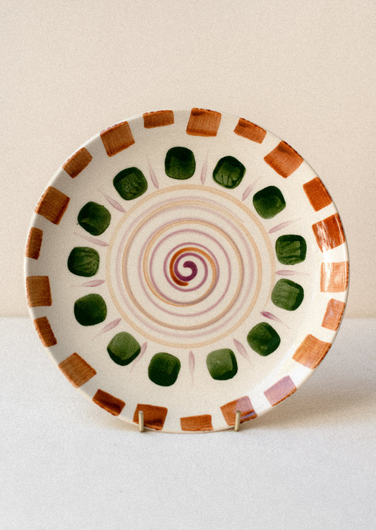 A plate with hand painted geometric swirl and square pattern in brown, green and purple.