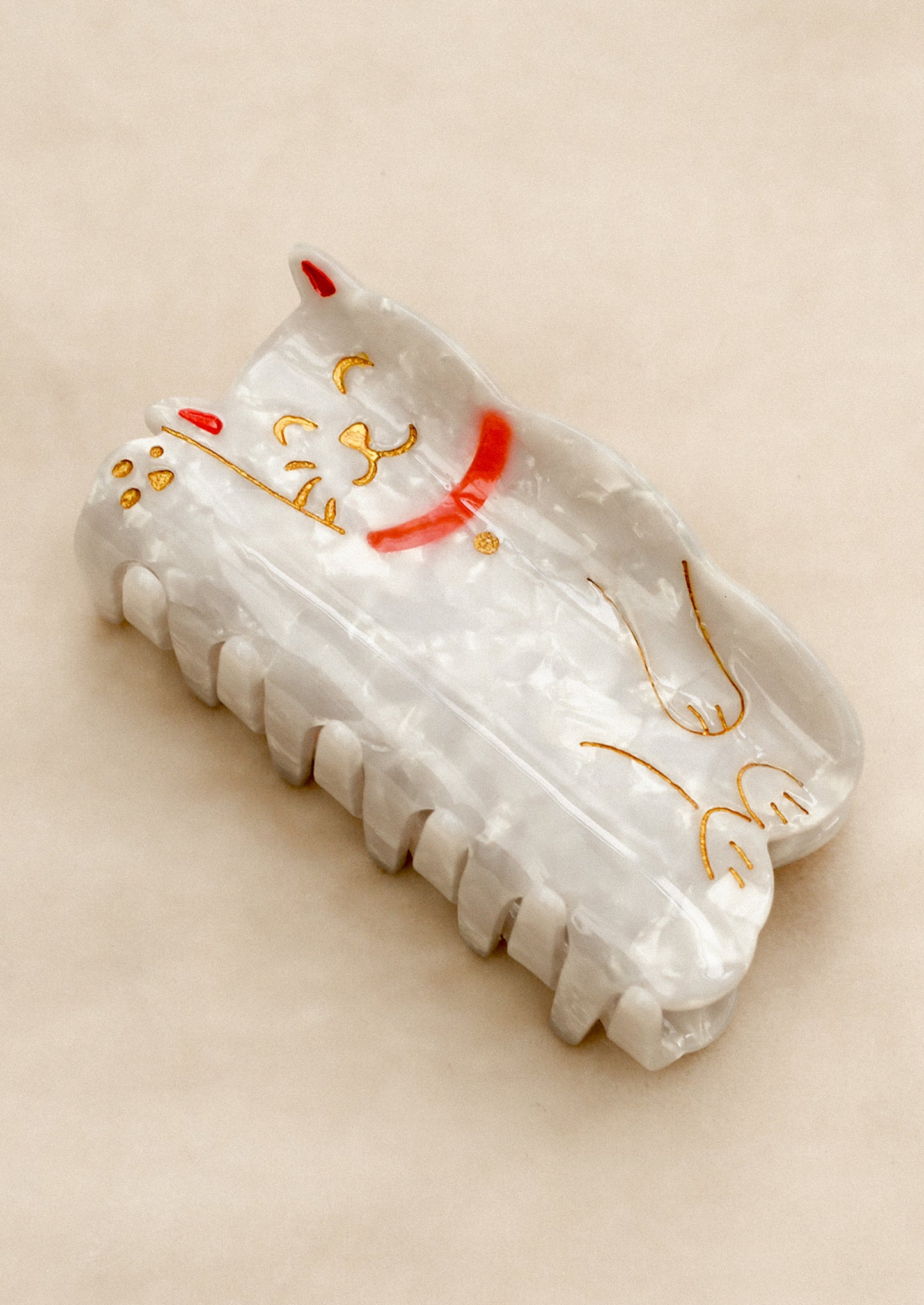 A hair claw in shape of Chinese lucky cat in white with red and gold detailing.