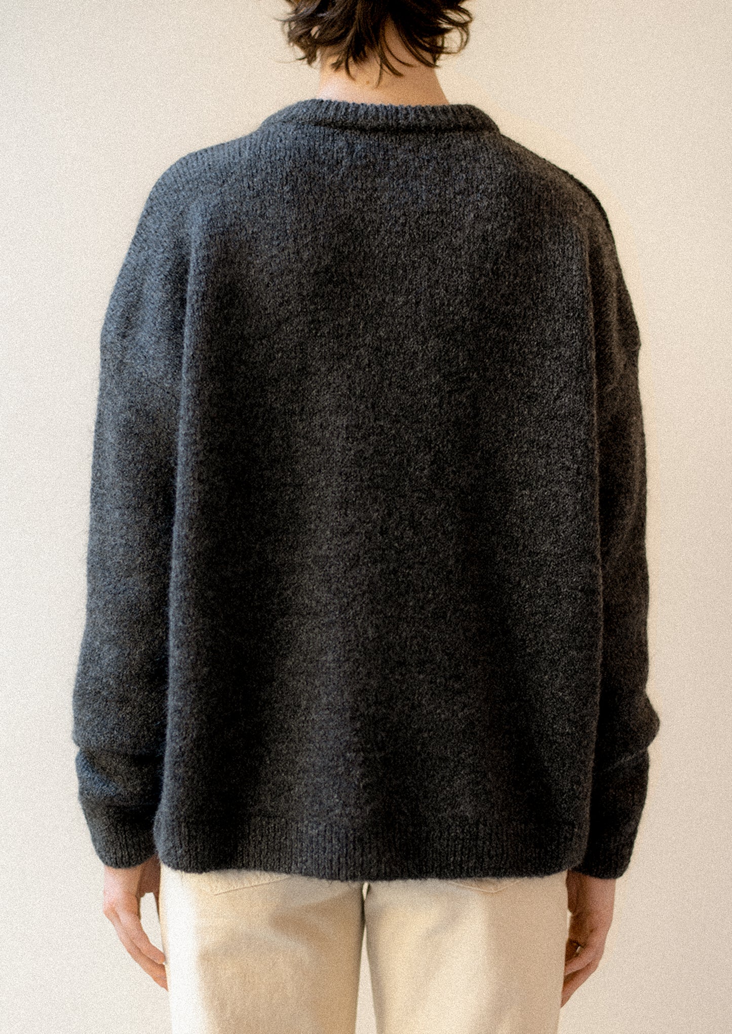 A woman wearing a charcoal long sleeve sweater with round neckline.