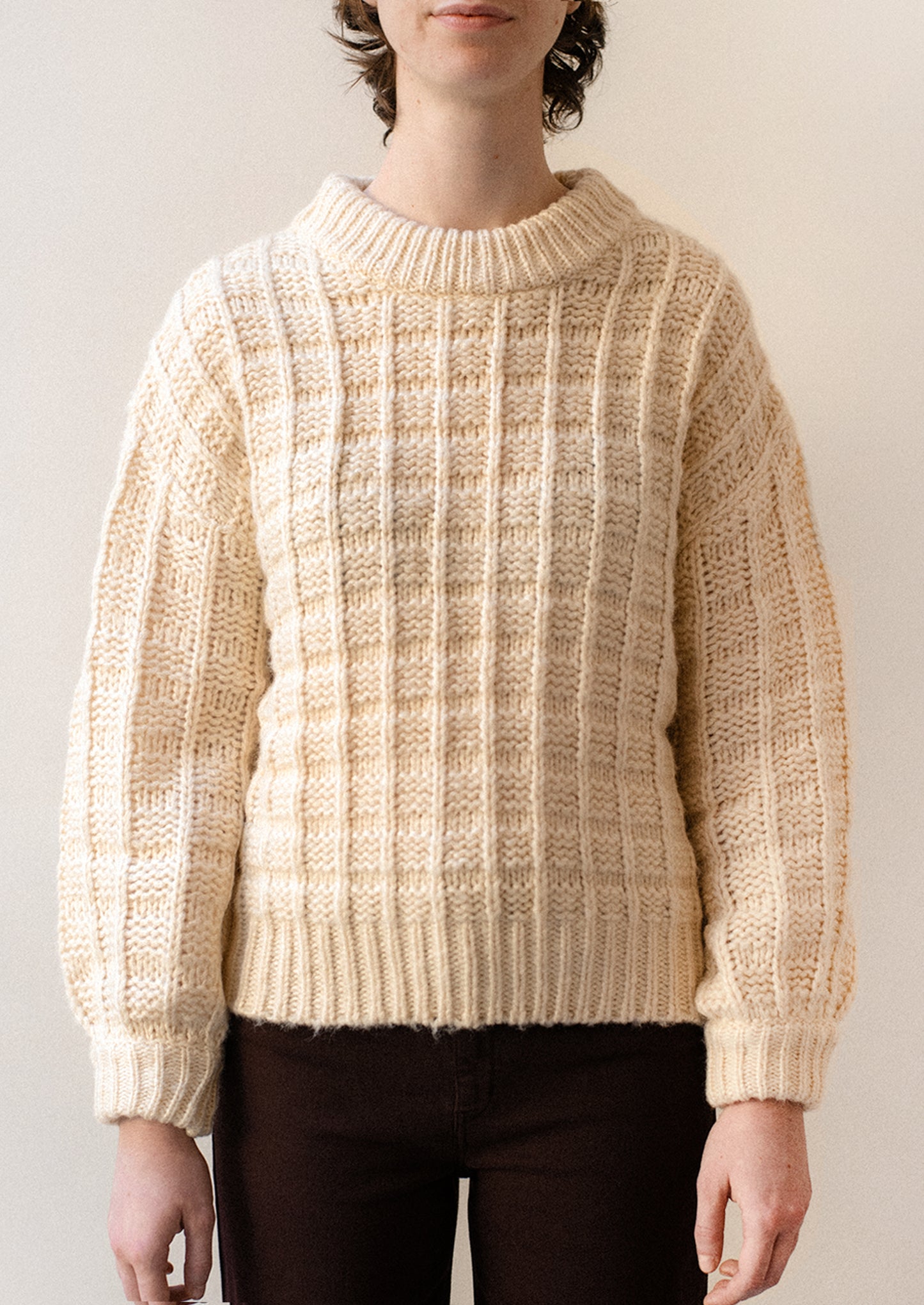 A person wearing a chunky waffle knit sweater in cream.