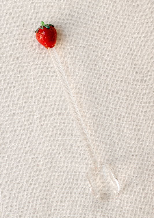 A clear glass spoon stirrer with red lampwork glass strawberry at end.