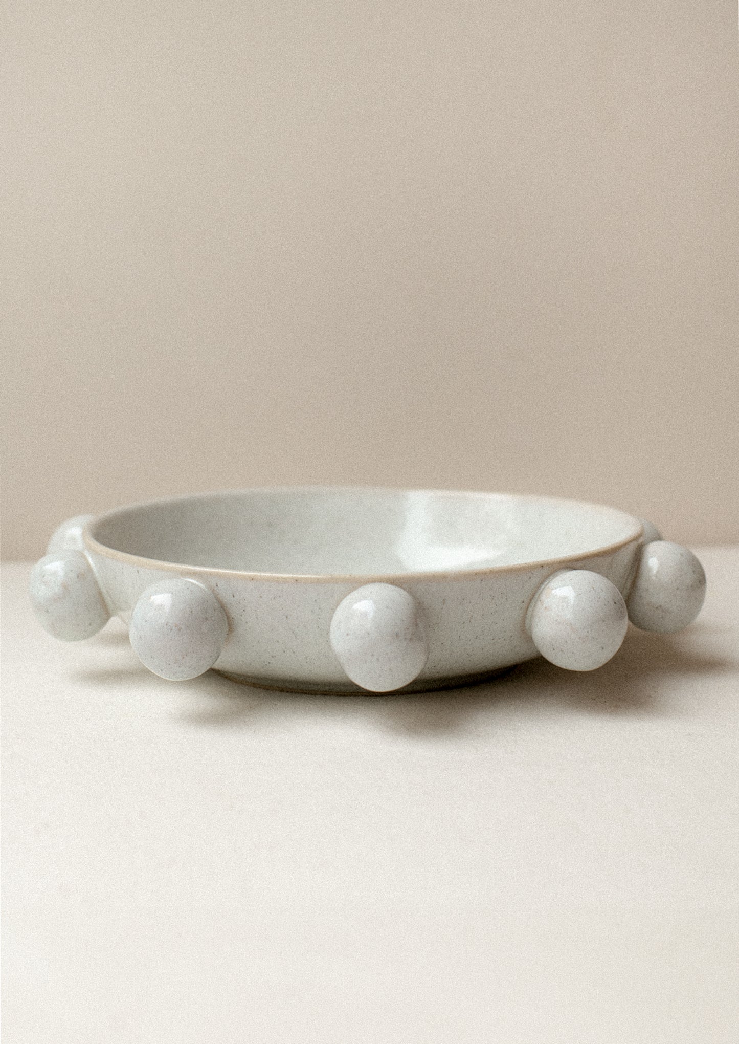 A shallow bowl in grey speckled ceramic with decorative ball detail around outside.