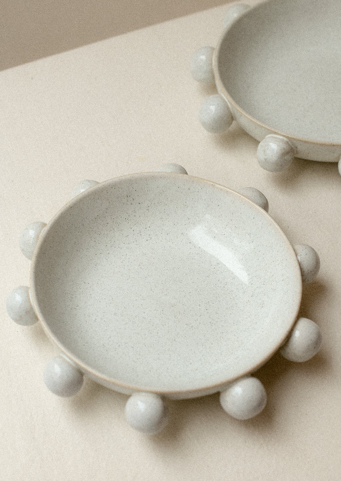 A shallow bowl in grey speckled ceramic with decorative ball detail around outside.