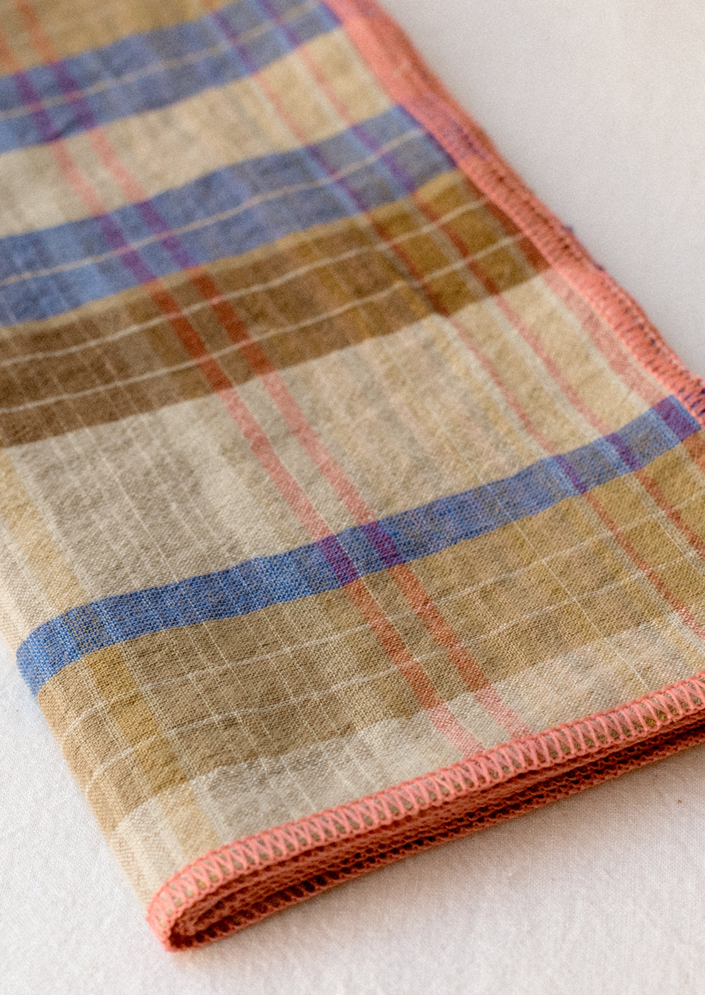 A pair of linen napkins in brown and blue plaid with pink stitch trim.