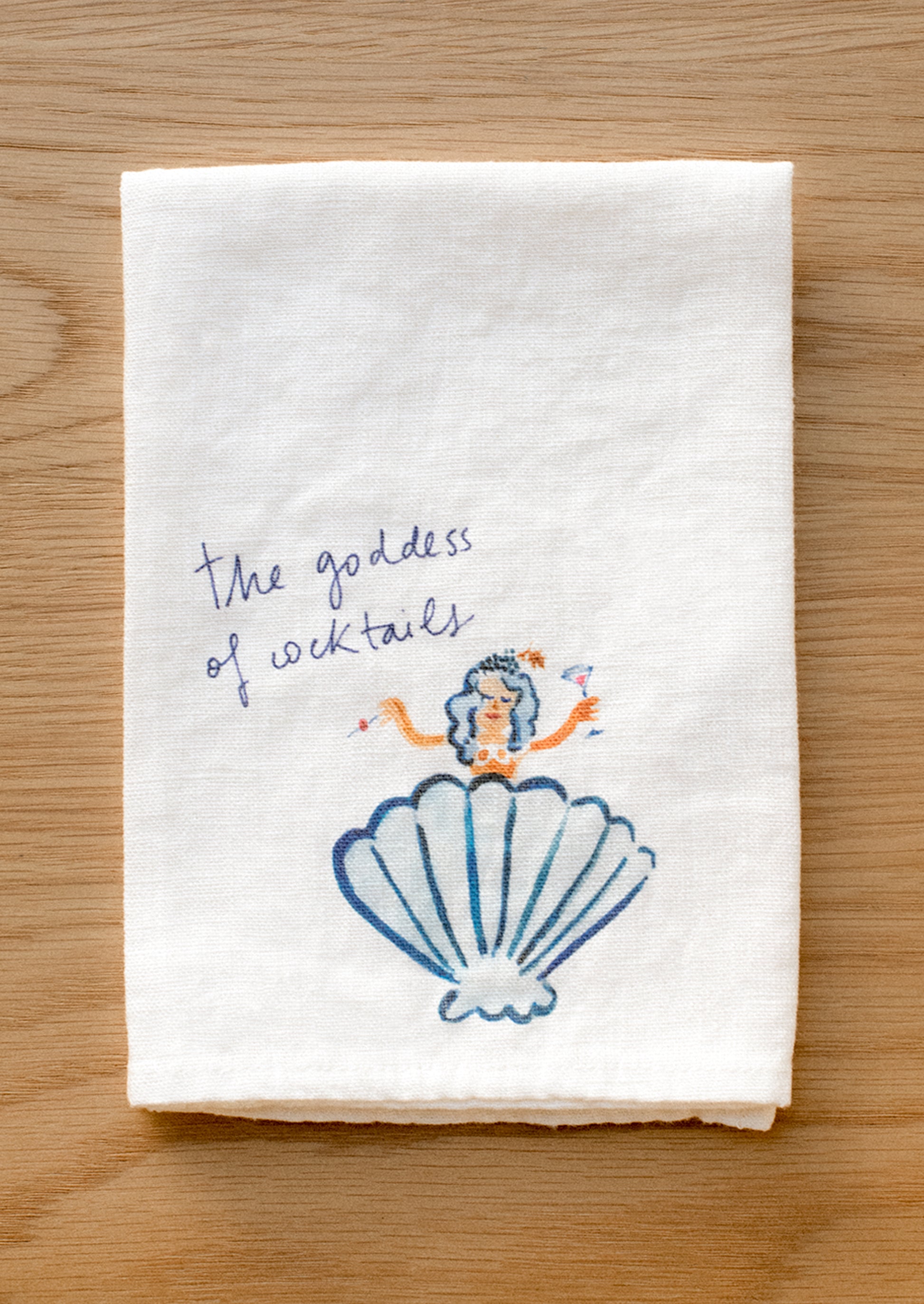 A white linen napkin with graphic detail of mermaid in shell.