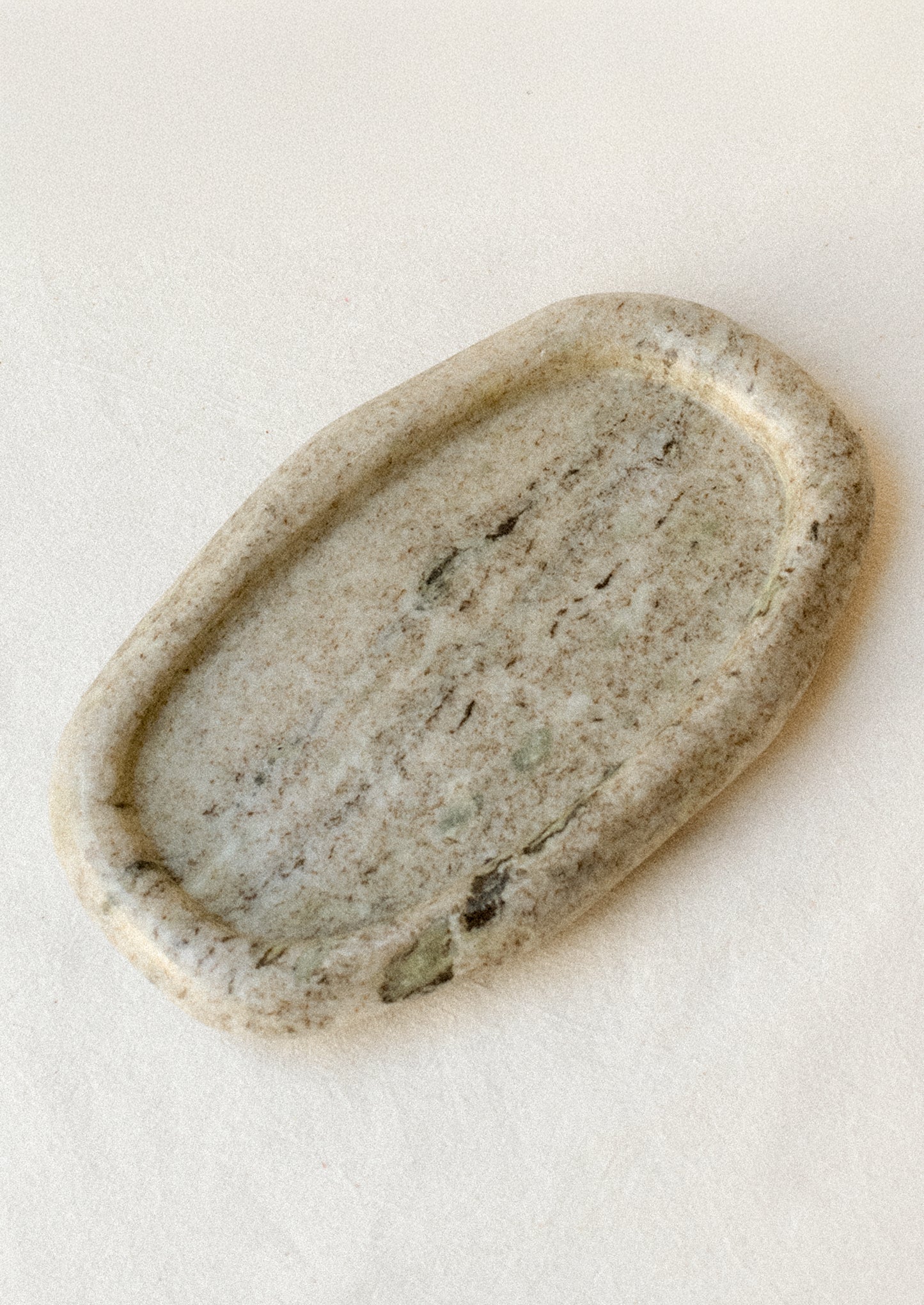 An oval shape catchall tray made of variegated marble, with asymmetrical, amoeba-like shape, with raised puffy rim.