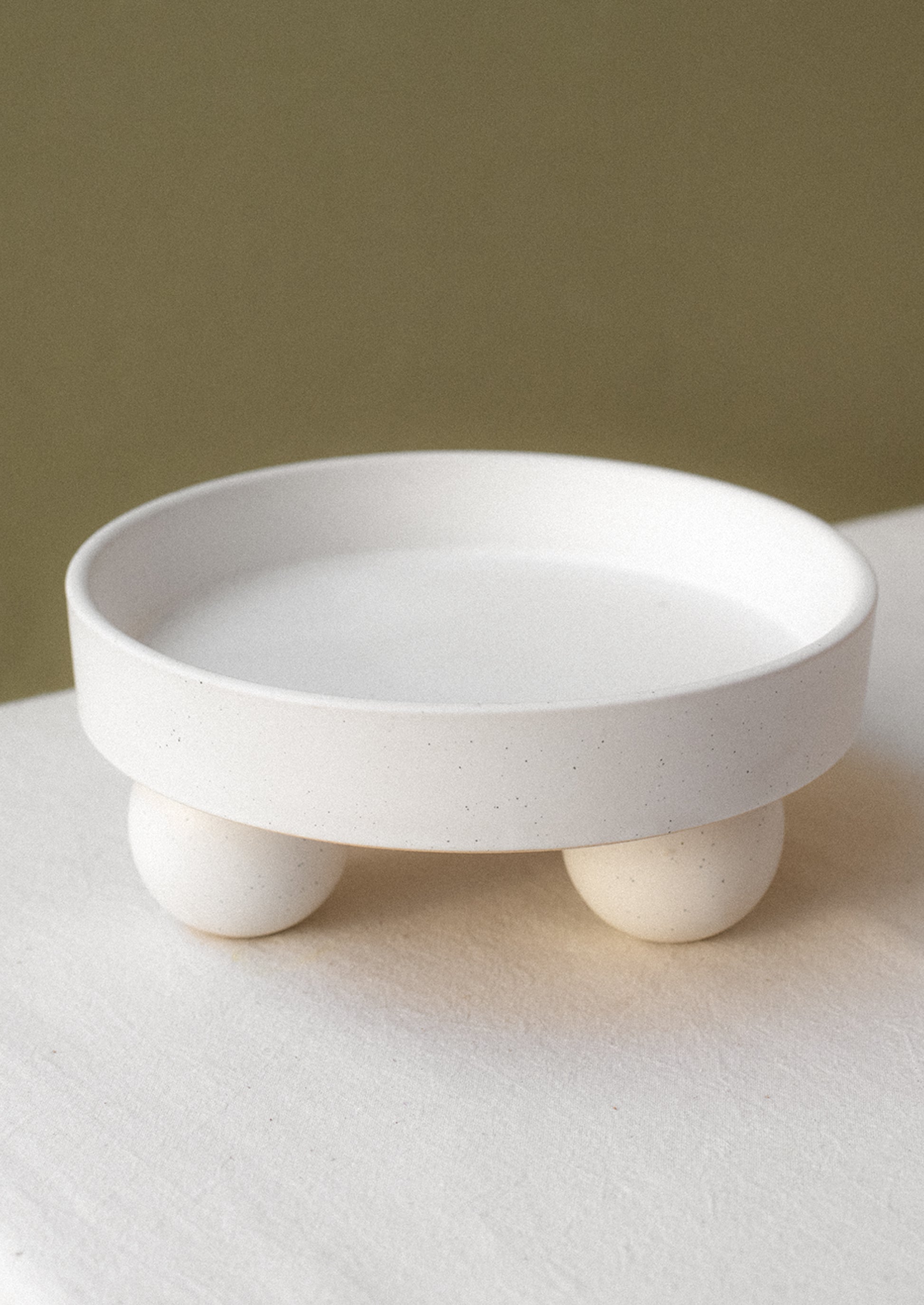 A round, rimmed riser in speckled white ceramic with ball shaped feet.