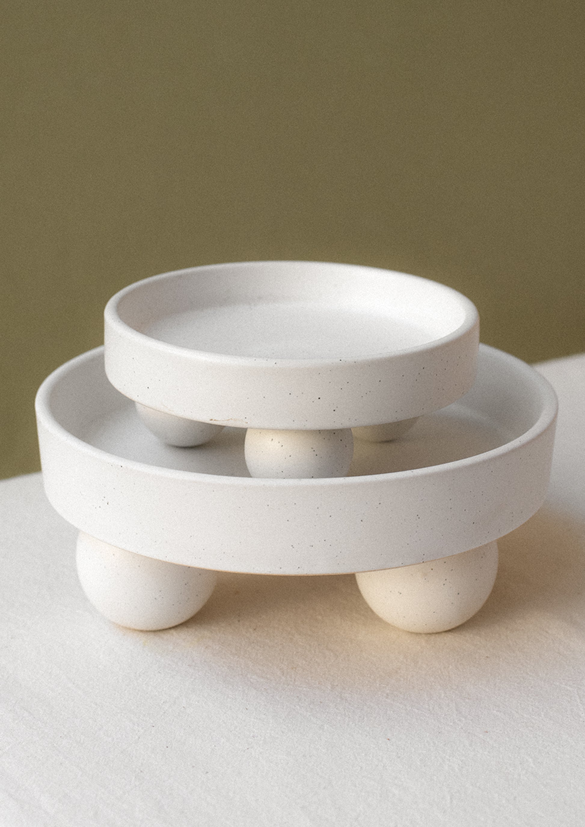 Round, rimmed risers in speckled white ceramic with ball shaped feet.