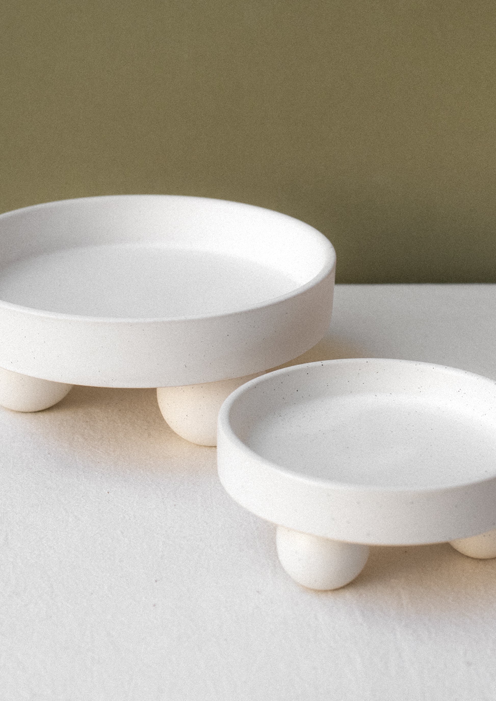 Round, rimmed risers in speckled white ceramic with ball shaped feet.