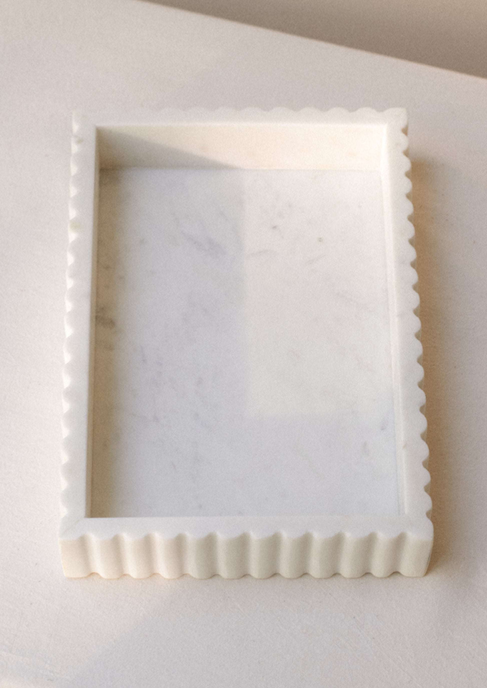 A rectangular tray in white marble with inset center, raised scallop edge border.