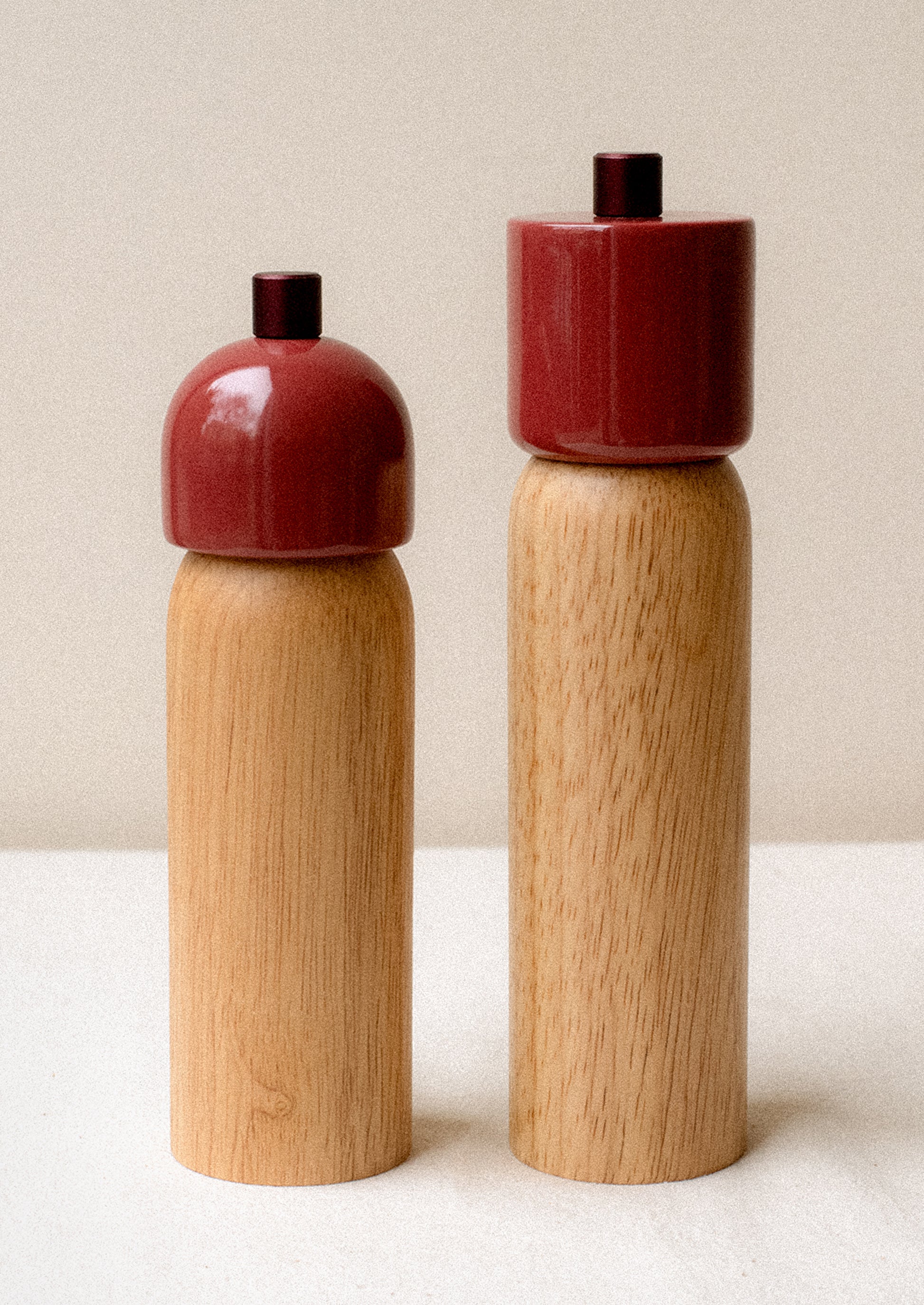 A pair of rubberwood spice grinders with lacquered dark red top.