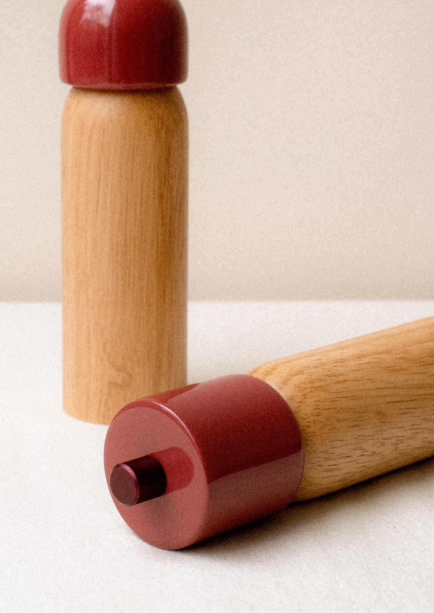 A pair of rubberwood spice grinders with lacquered dark red top.