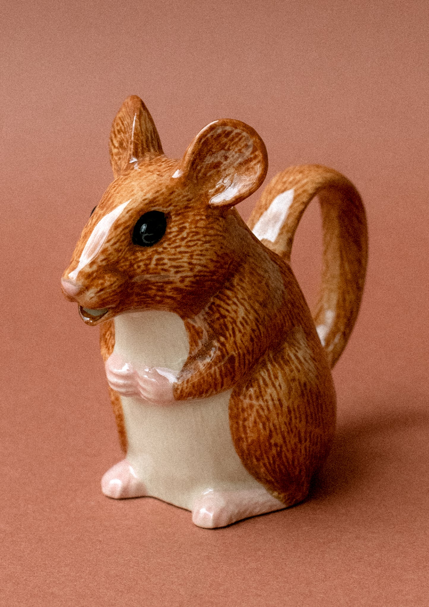 A tiny ceramic creamer pitcher with handle in the shape of a small brown wood mouse.