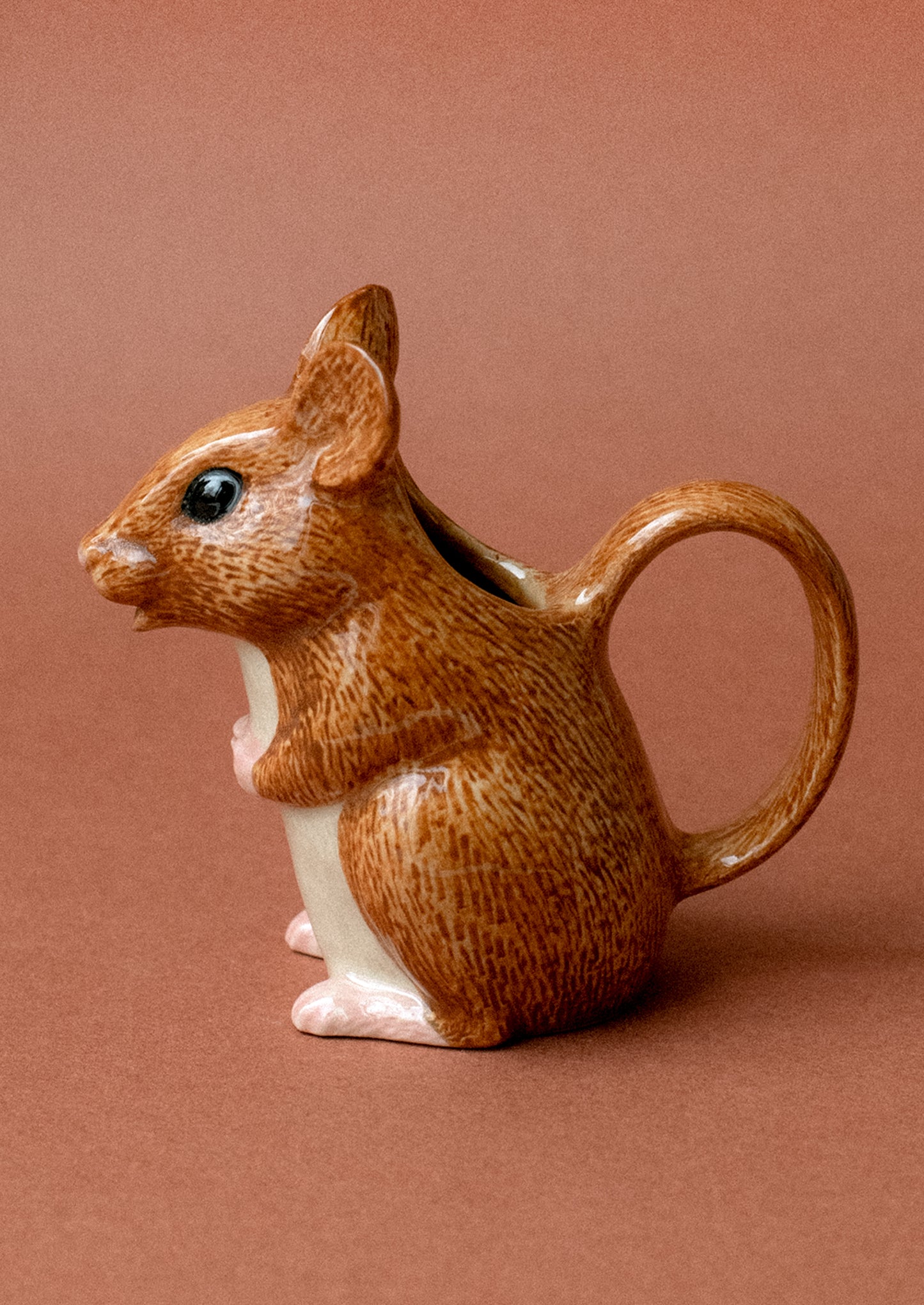 A tiny ceramic creamer pitcher with handle in the shape of a small brown wood mouse.