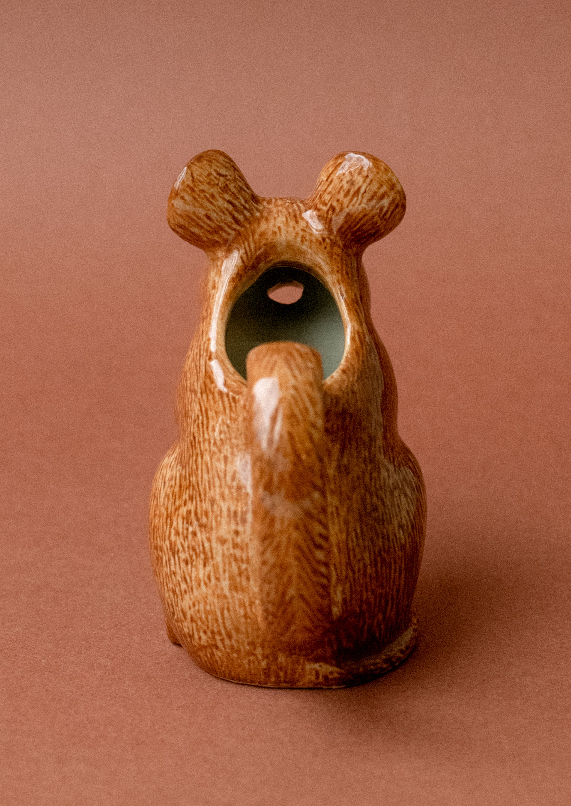 A tiny ceramic creamer pitcher with handle in the shape of a small brown wood mouse.