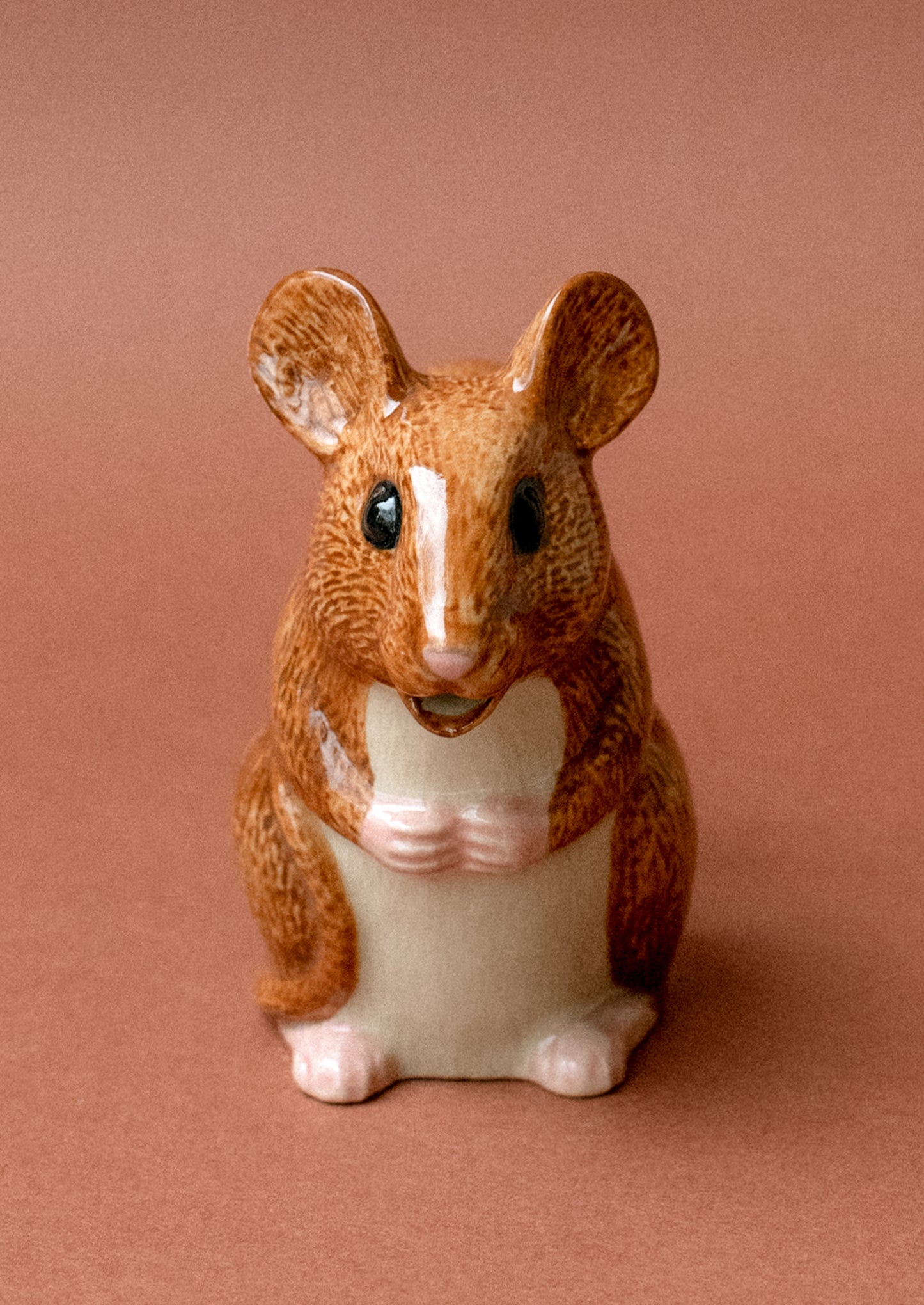 A tiny ceramic creamer pitcher with handle in the shape of a small brown wood mouse.