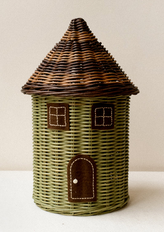 A round rattan basket in the shape of a house, with window and door detailing, lid is the roof.