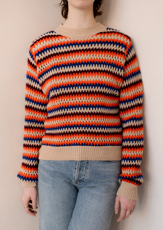 A woman wearing a crochet knit striped sweater in cream with orange, maroon and blue stripes.