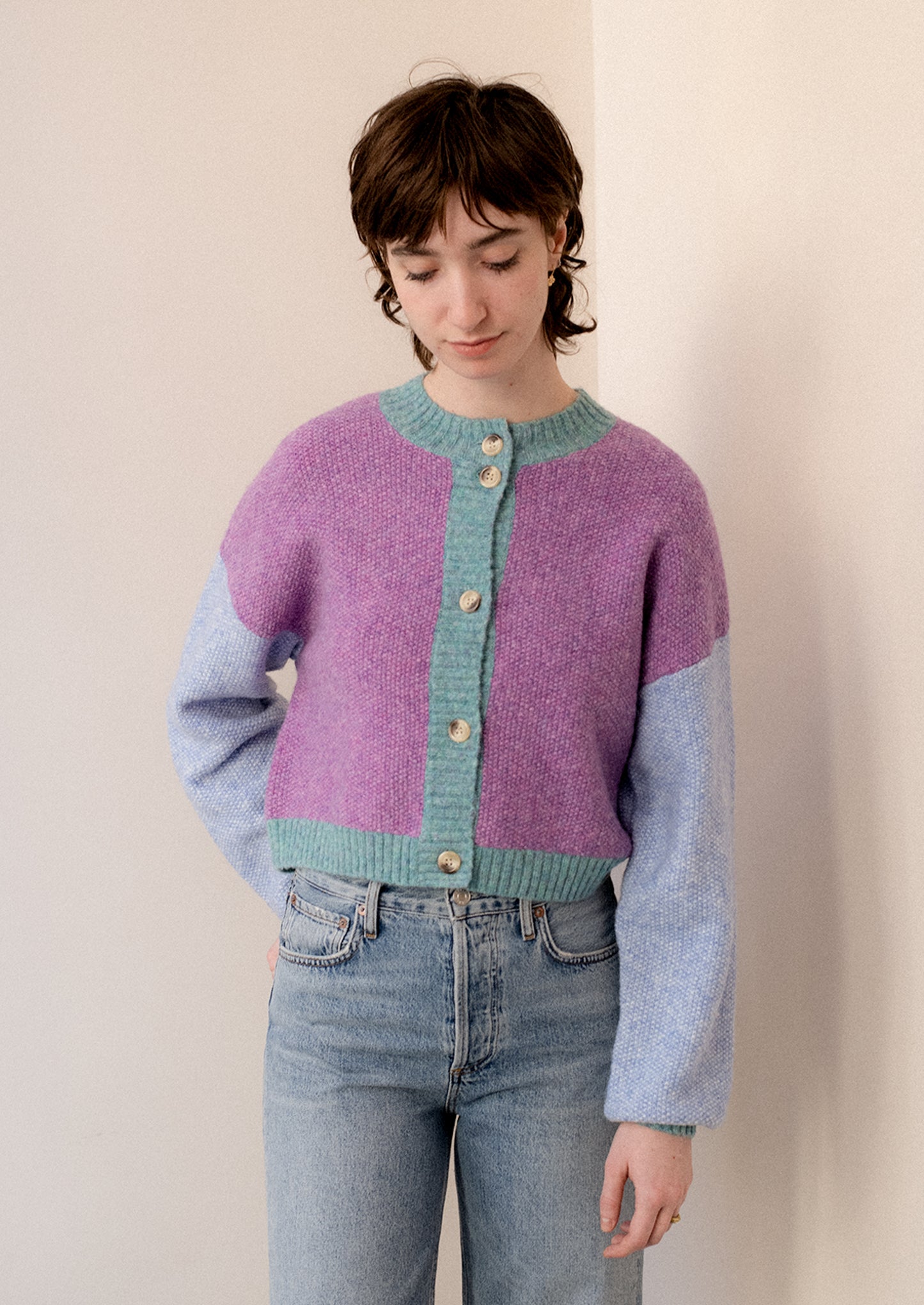 A woman wearing a colorblocked cardigan sweater in aqua, periwinkle and purple.