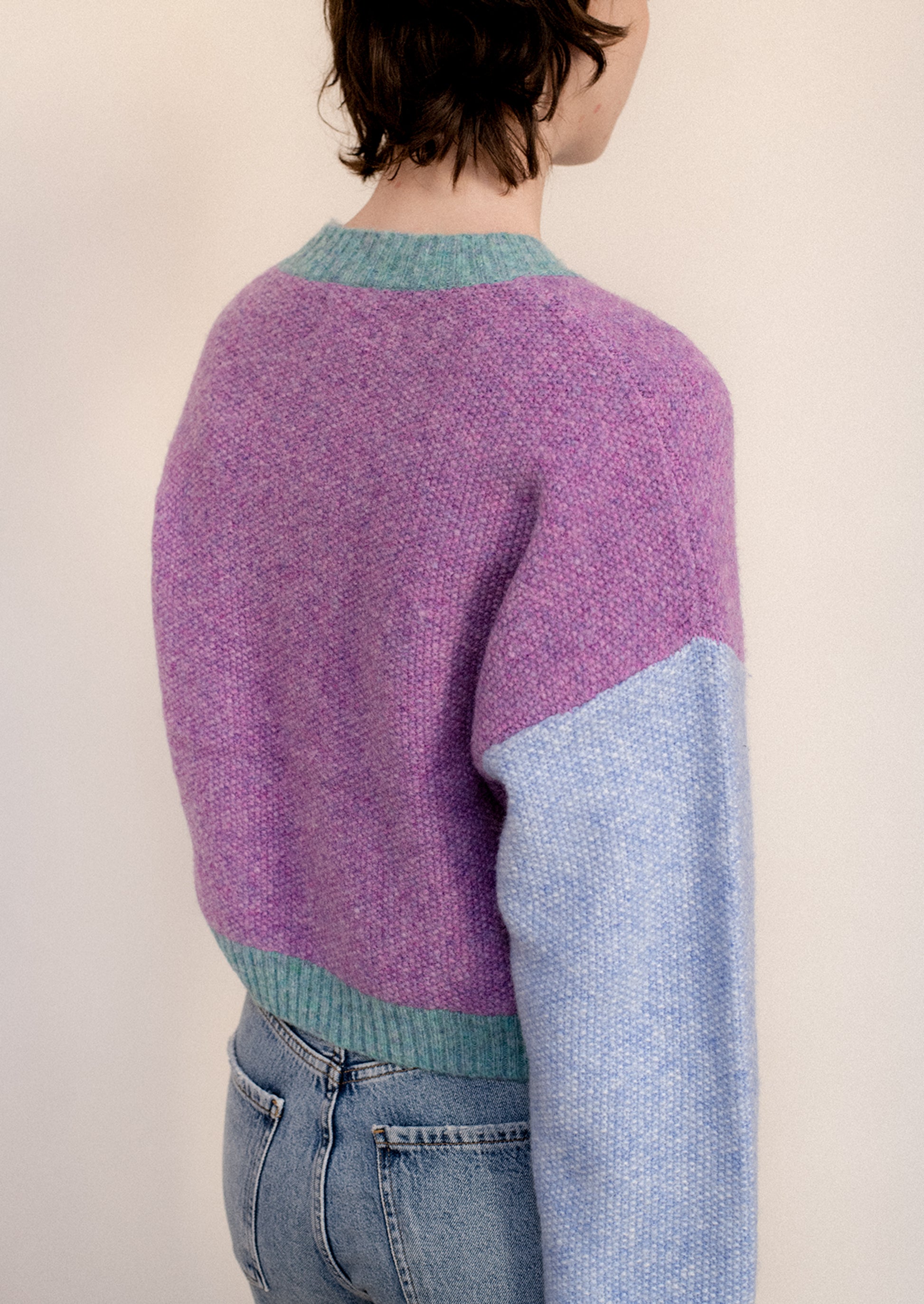 A woman wearing a colorblocked cardigan sweater in aqua, periwinkle and purple.