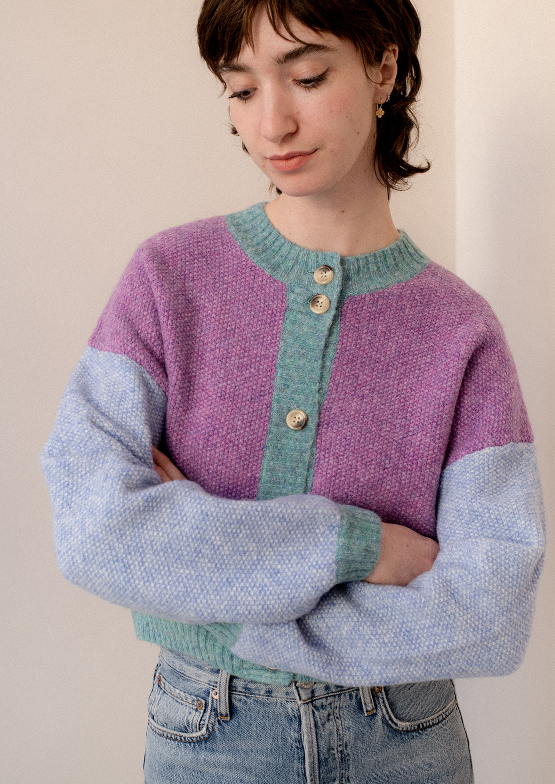 A woman wearing a colorblocked cardigan sweater in aqua, periwinkle and purple.