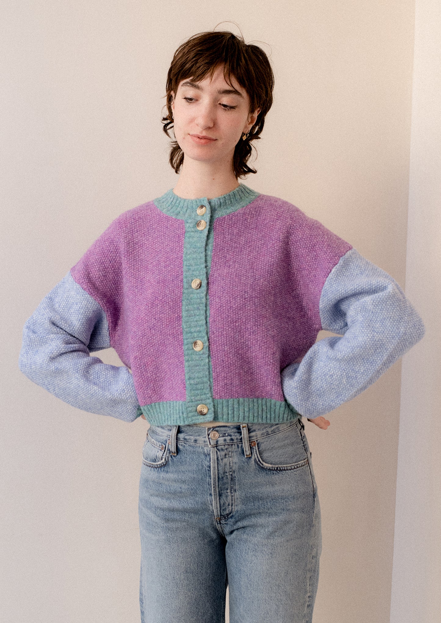 A woman wearing a colorblocked cardigan sweater in aqua, periwinkle and purple.