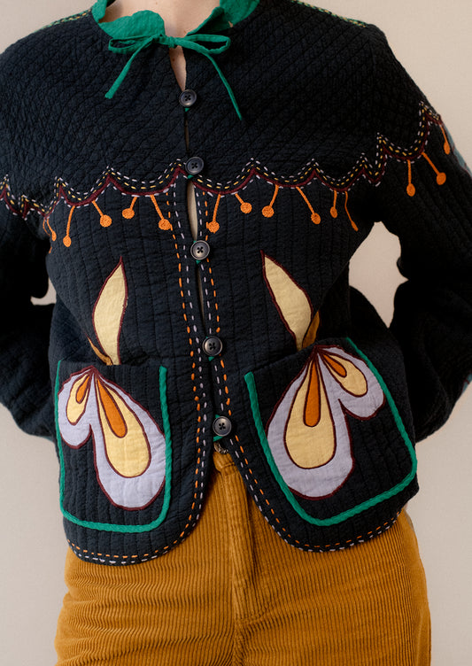 A woman wearing a navy embroidered jacket with whimsical abstract embroidery throughout.