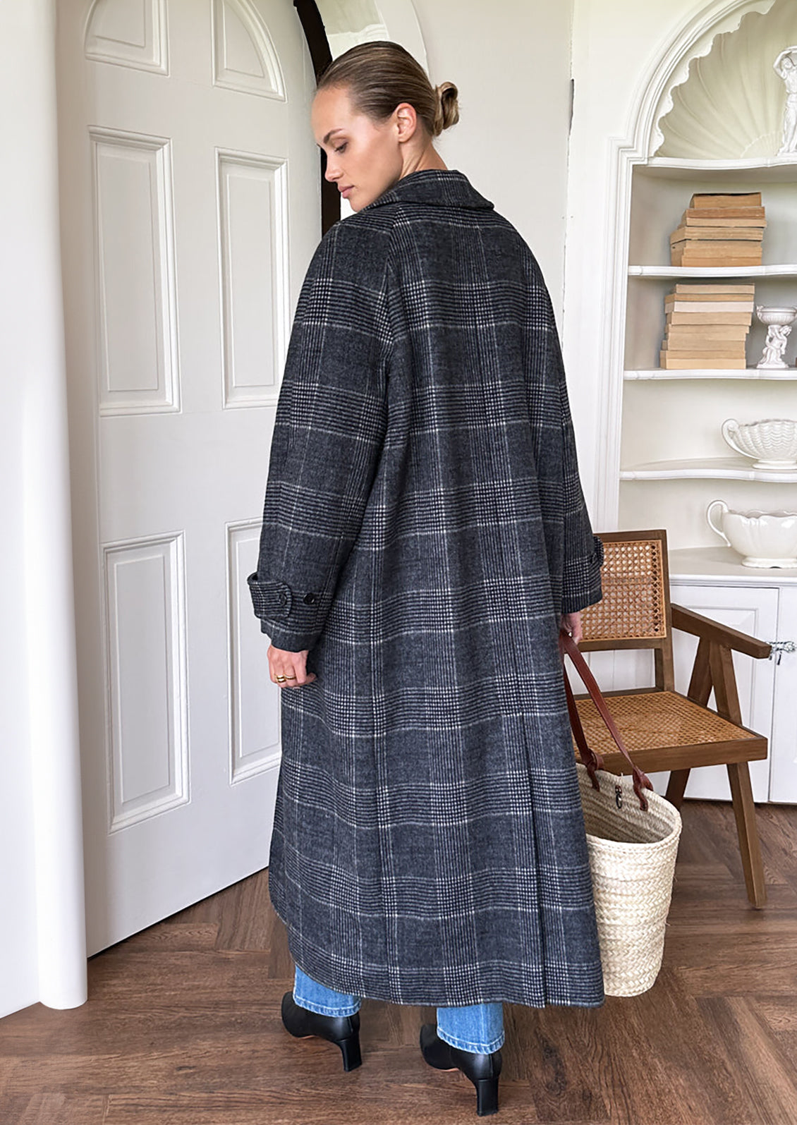 A woman wearing a long wool overcoat in charcoal and white plaid pattern.