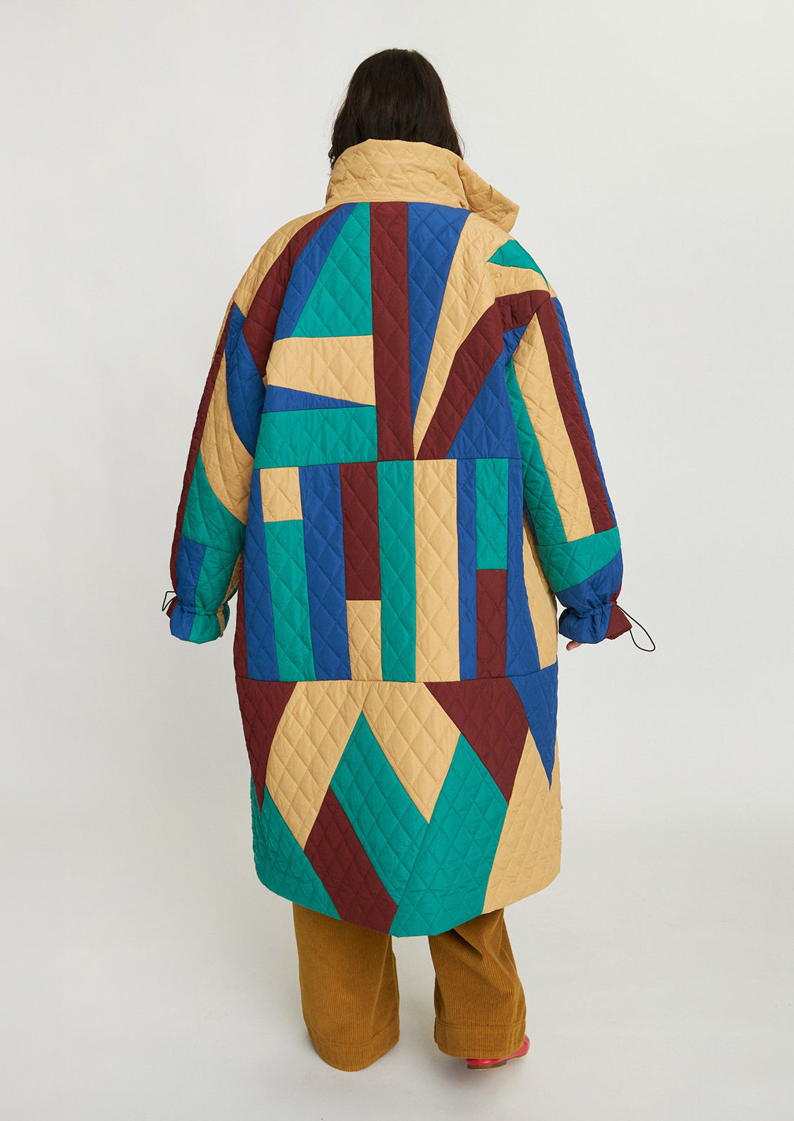 A woman wearing a geometric patchwork quilted coat in wine, teal, beige and blue.