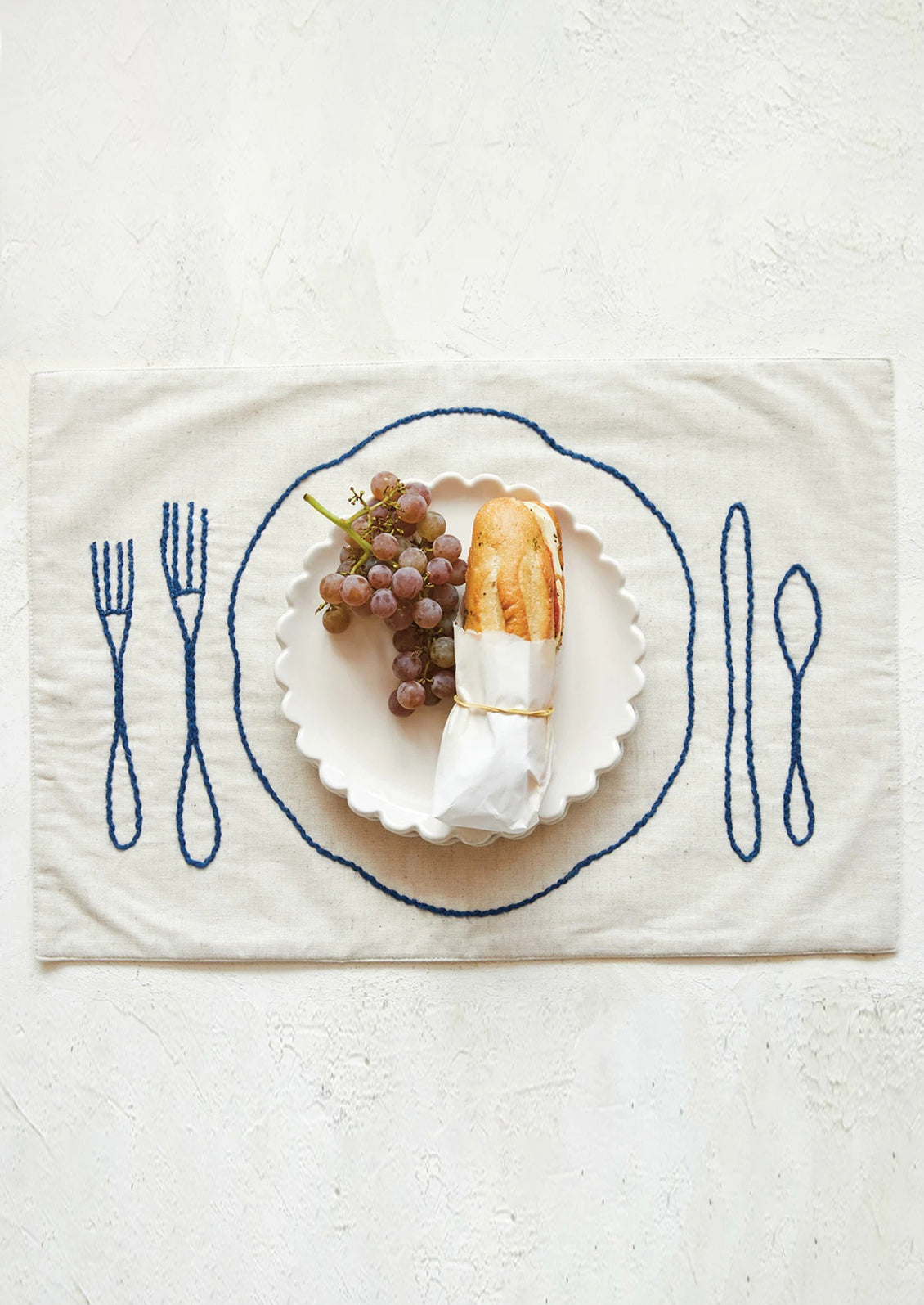 An off-white linen-cotton placemat with navy blue plate and silverware embroidery.