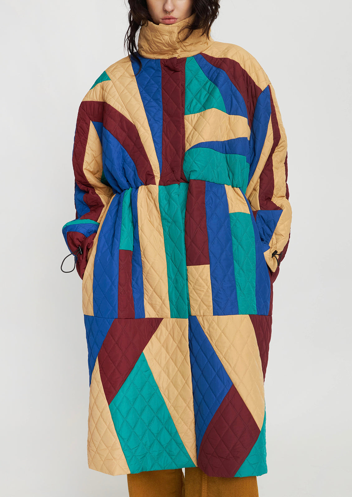 A woman wearing a geometric patchwork quilted coat in wine, teal, beige and blue.