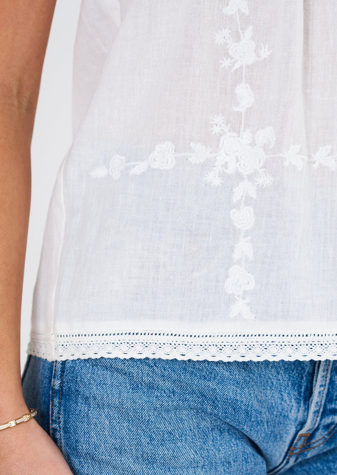 A woman wearing a white cami with tonal floral embroidery.