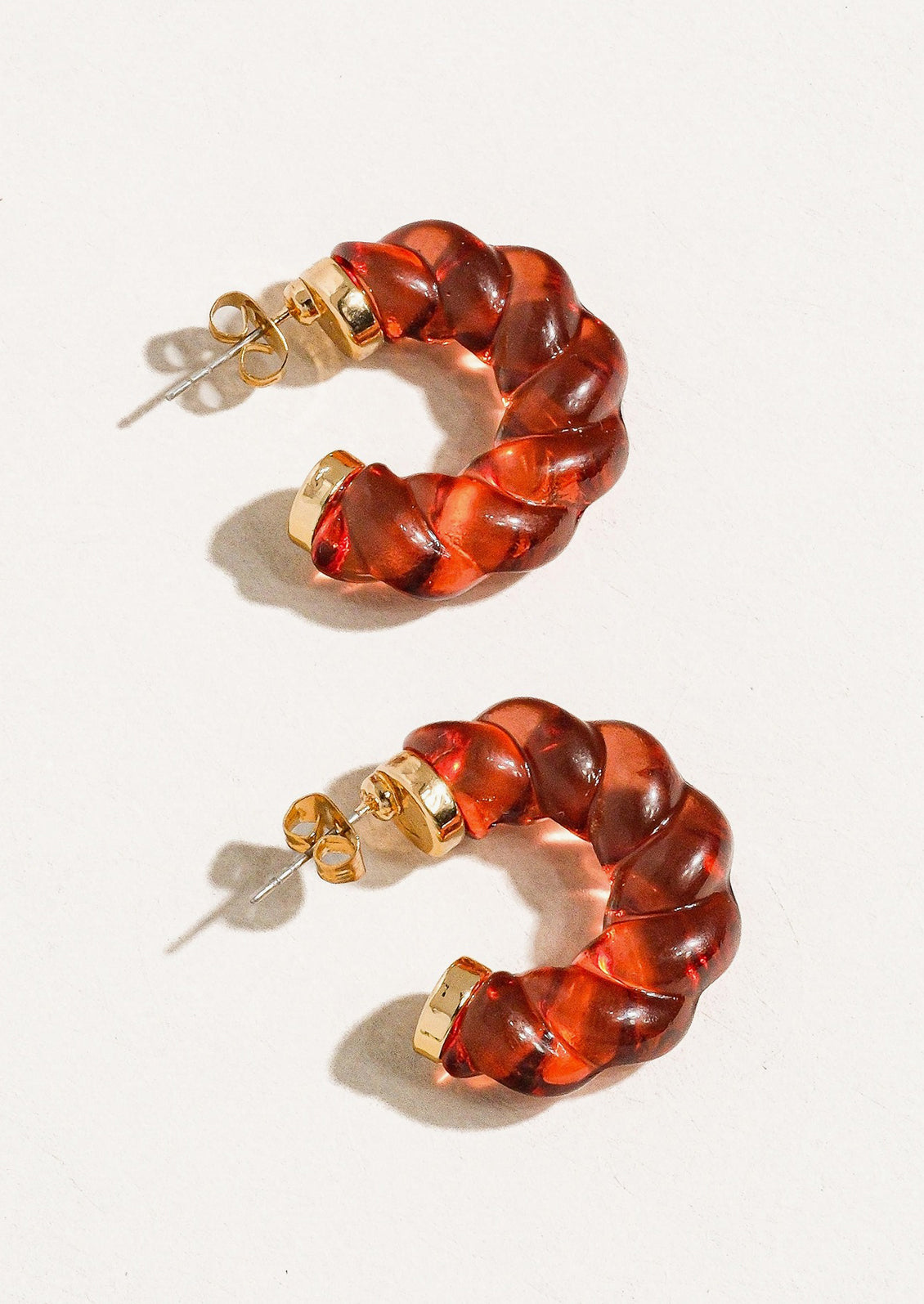 A pair of transparent lucite hoop earrings with spiral twist texture in ruby red.