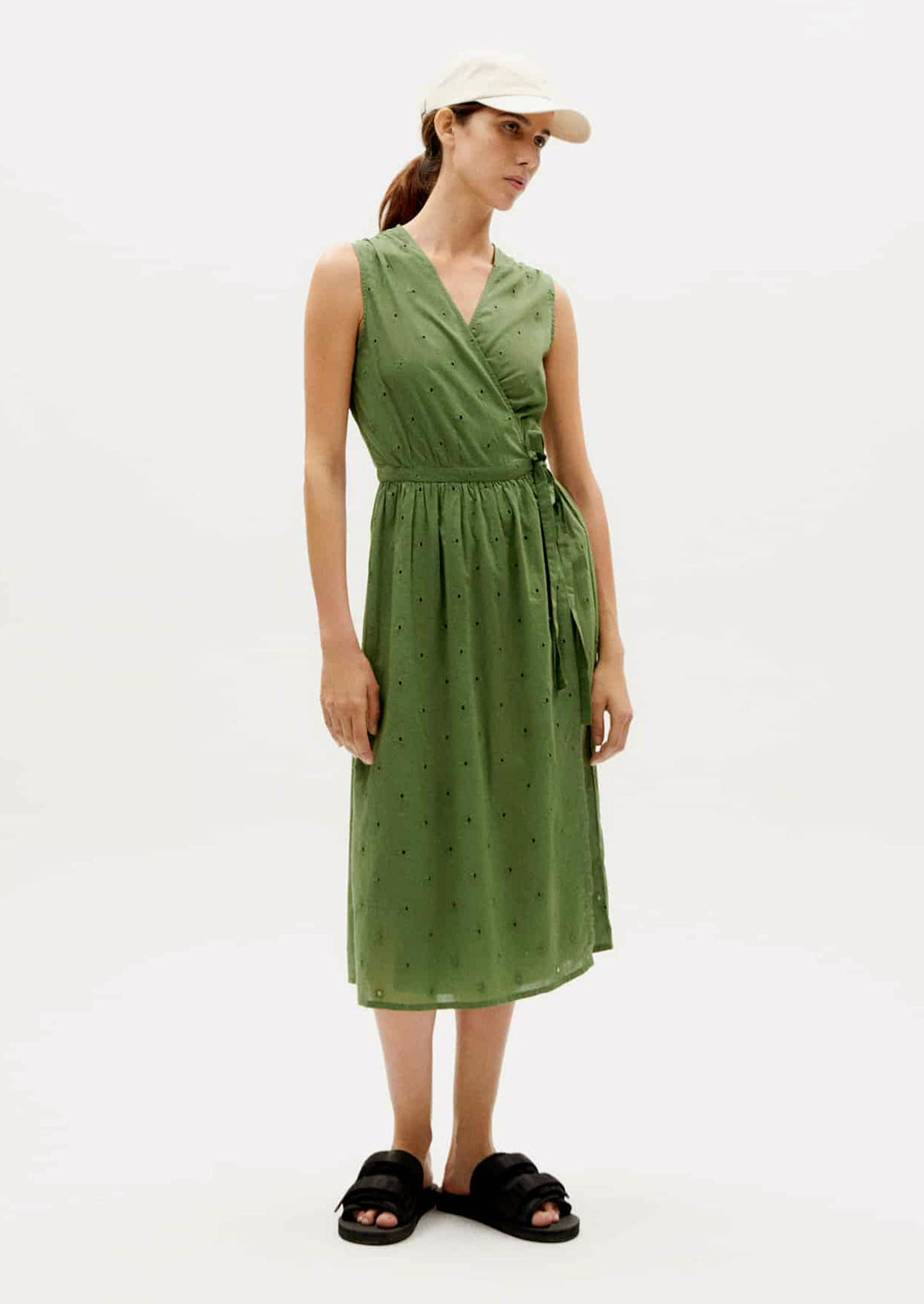 A woman wearing a green sleeveless midi wrap dress.
