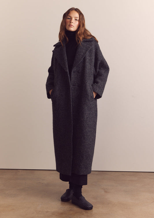 A woman wearing a long wool coat in dark grey speckled wool.