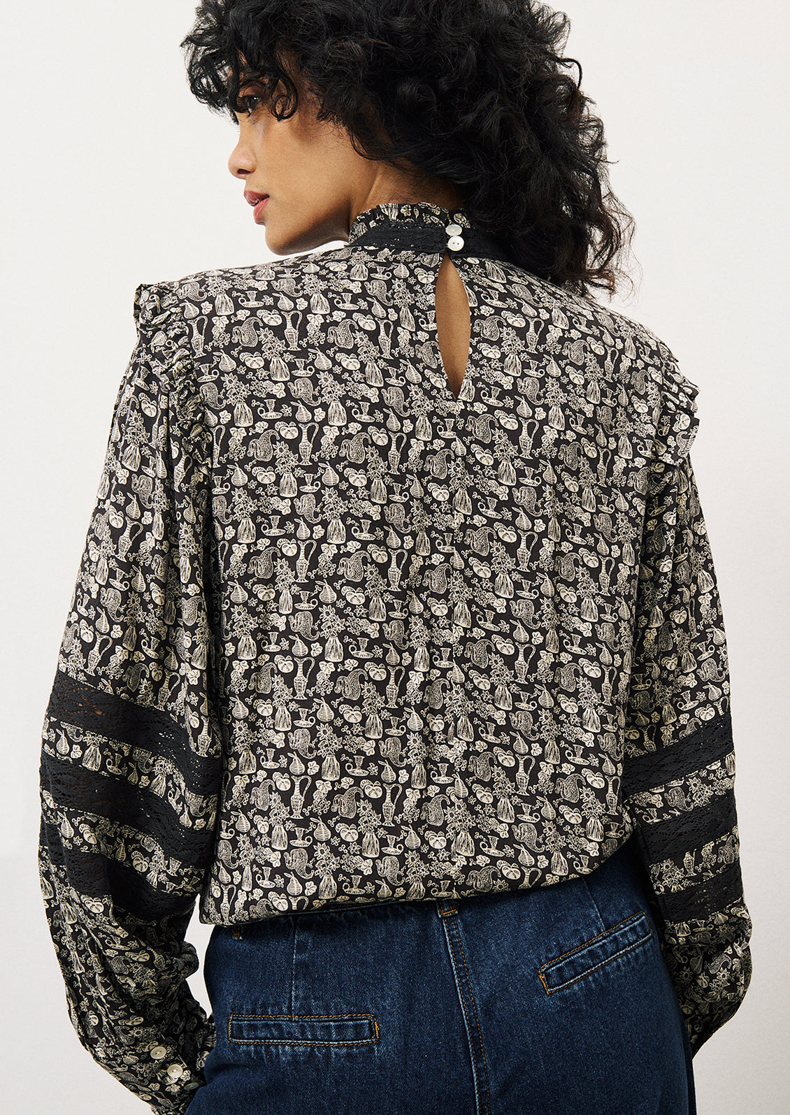 A woman wearing a printed blouse in dark blue with small white pattern of vases and flowers.