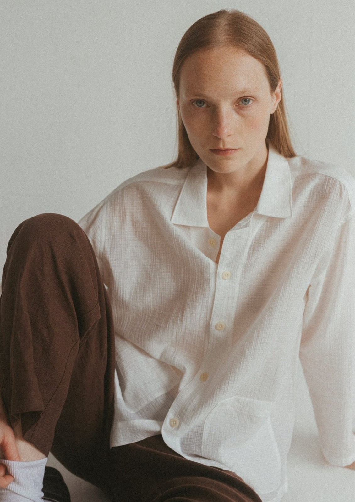 A woman wearing a semi-sheer, gauze-textured white button front shirt.