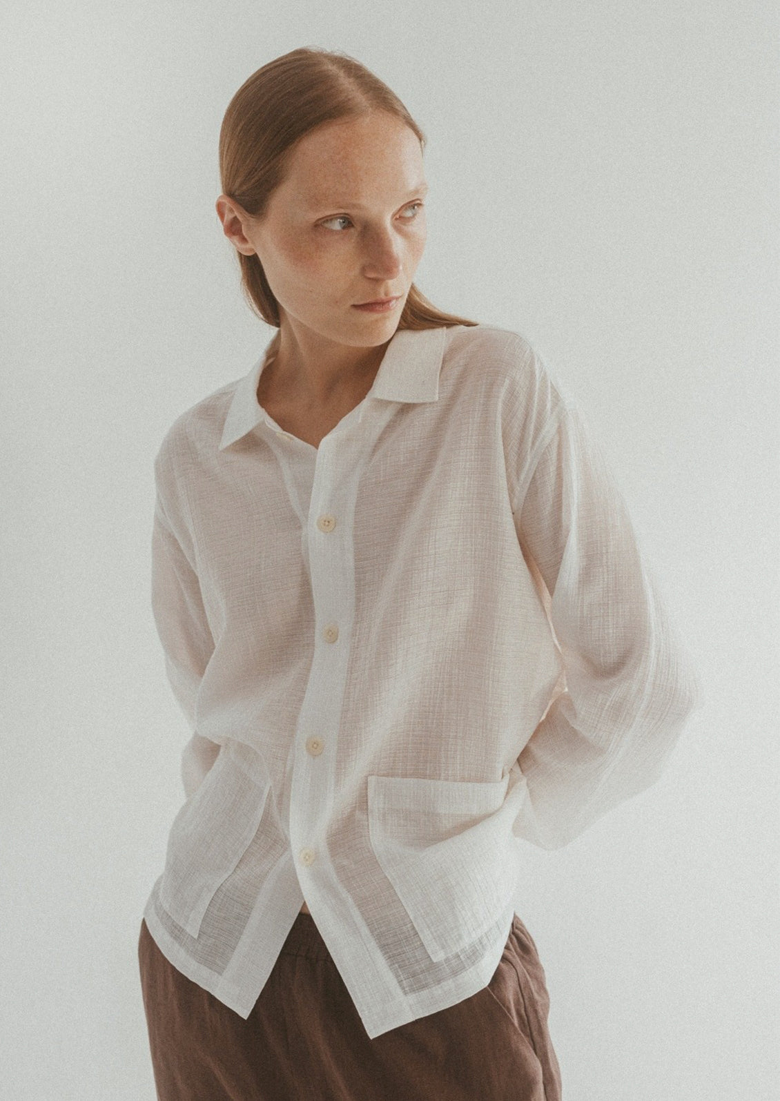 A woman wearing a semi-sheer, gauze-textured white button front shirt.
